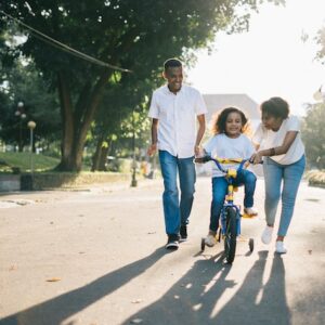 Family smiling in street helping young child to ride bike