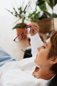 woman sitting down holding out glasses looking stressed